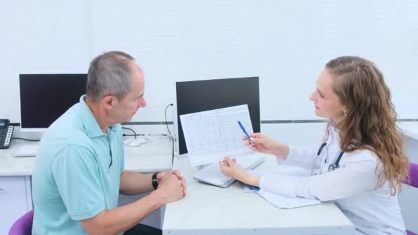 Kardiolog Analizuje Wyniki Elektrokardiogramu Serca Starszego Mężczyzny Podczas Konsultacji Konsultacja — Wideo stockowe