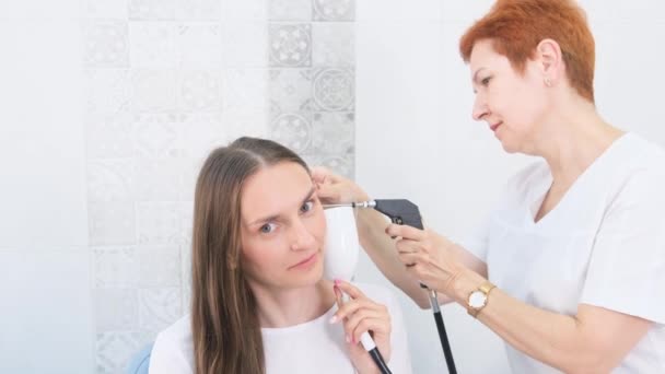 一位耳鼻喉科医生使用现代医疗设备为一位年轻的成年妇女洗耳恭听和清除耳垢 保健和医药的概念 — 图库视频影像
