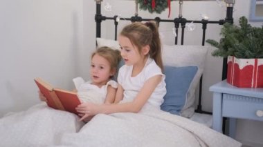 İki küçük kız aynı yatakta bir kitap okuyor.