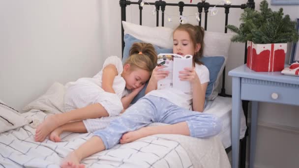 女の子は同じベッドで寝る前に妹のために本を読みます — ストック動画