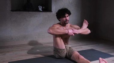 Çıplak gövdesiyle yoga yapan genç bir adam yoga minderinde egzersiz yapıyor..