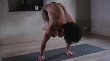 Çıplak gövdeli genç güçlü bir adam yoga yapıyor, ellerinin üzerinde esnek bir pozisyonda duruyor spor salonunda, denge egzersizleri yapıyor.