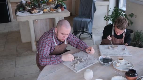 自閉症の症候群を持つ2人の若者と特別な生理学的発達を持つ2人は 家庭のワークショップで大きなテーブルに座って粘土モデリングに従事しています 優れたモータースキルの開発 — ストック動画