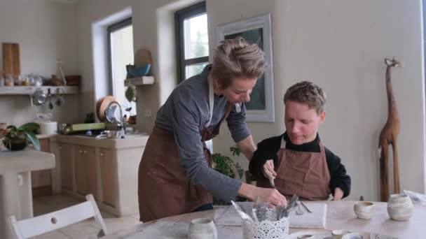 Волонтерка Допомагає Хлопцеві Фізичними Вадами Опанувати Моделювання Глини Сидячи Круглим — стокове відео