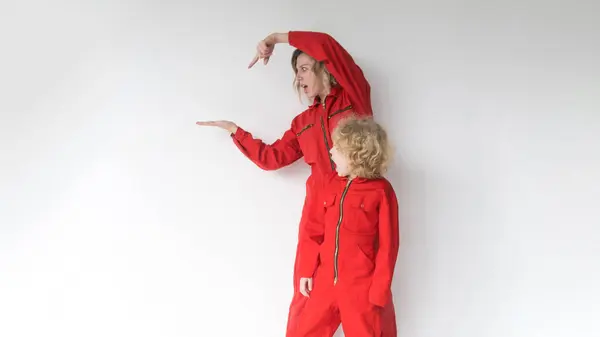 Een Positieve Blonde Met Een Jonge Zoon Rode Jumpsuits Wijst — Stockfoto