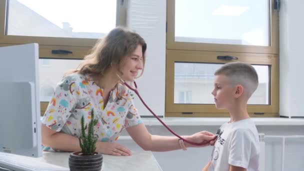 一个小男孩正在一家明亮的诊所里让一位面带微笑的儿科医生检查他的心率 — 图库视频影像