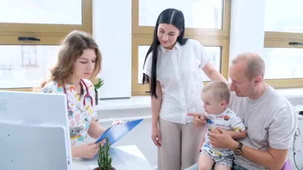 Par Med Liten Pjokk Fullfører Registreringsformaliteter Med Resepsjonist Pediatrisk Klinikk – stockvideo