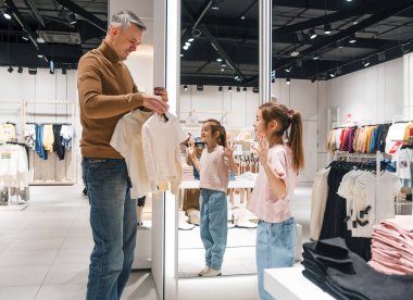 Bir baba genç kızına modern bir mağazada kıyafet seçmesinde yardım eder. Gülümsüyorlar ve hafta sonu alışverişlerinin tadını çıkarıyorlar..