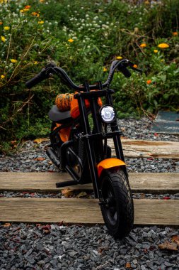 Portakal renkli bir çocuk bisikleti, motosiklet stili, kaprisli bir balkabağı ile süslenmiş, genç kaşifler için eğlenceli ve maceralı bir sonbahar gezisini simgeliyor.