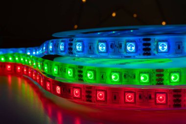Set of colorful chasing LED strips with bright neon red green and blue lights placed on table in dark room