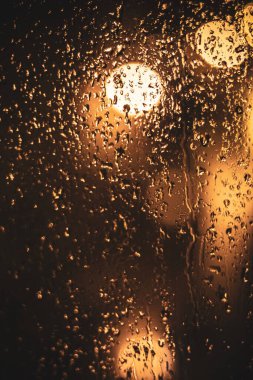 Karanlık bir akşamda parlayan parlak bokeh ışıklarına su damlalarıyla şeffaf ıslak cam yüzey