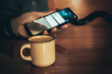 Tanımlanamayan yaşlılardan mesaj ekranına bakarken arka planda bulanık bir şekilde bir fincan sıcak kahveyle oturanlardan.