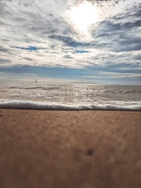 Parlak bulutlu gökyüzüne karşı kumlu deniz kıyısına vuran köpüklü dalgaların inanılmaz manzarası