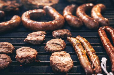 Canlı sosis çeşitleri ve sığır köfteleri mükemmelce kızartılıyor, yaz aylarında nefis bir açık hava pişirme deneyimi sergiliyor..