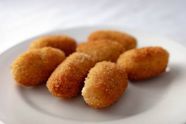 Ağız sulandıran beyaz tabağa istiflenmiş altın-kahverengi kroketler, çıtır çıtır dokularını sergiliyor, yemek fotoğrafçılığı ve mutfak sanatı için mükemmel..