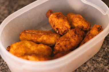 Altın sarısı ev yapımı kroketler şeffaf bir plastik kap içinde düzgünce dizilmiş. Sıcak bir mutfak ortamında yakın çekim, ev yemeklerini, yemek hazırlıklarını ya da geleneksel İspanyol yemeklerini göstermek için mükemmel.. 