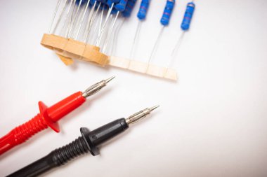  Kırmızı ve siyah çoklu metre test sondalarının üst görüntüsü beyaz bir yüzeyde mavi elektronik rezistansların yanında. Elektronik, devre testi, elektrik tamiri ve teknoloji kavramlarını göstermek için mükemmel..