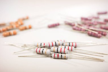  Beyaz bir yüzeye dağılmış farklı renk bantlı çeşitli karbon film dirençlerinin makro çekimi, teknik çeşitliliklerini vurguluyor..