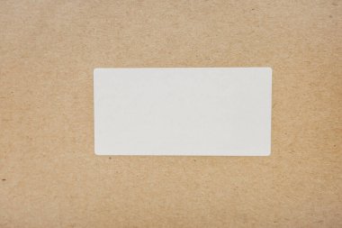 Karton bir yüzeye yerleştirilmiş tek boş beyaz dikdörtgen yapıştırıcı etiketi. Ürün markalaşması, ambalaj tasarımı ve tanımlama kavramları için mükemmel..