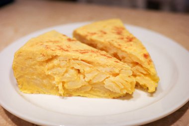 Tortilla de patatas olarak bilinen ev yapımı İspanyol patates omletinin yakın çekimi, beyaz bir tabakta üçgen porsiyonlar halinde servis edilir. İspanya 'da popüler geleneksel yemek, genellikle tapas ya da ana yemek olarak yenir..