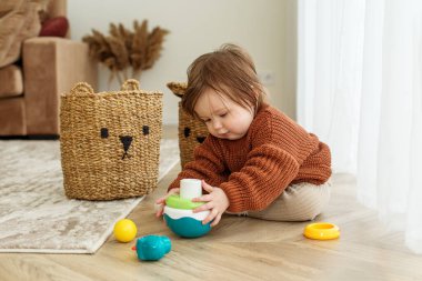 Küçük çocuk odada yerde oyuncaklarla oynuyor. Çocukluk, anaokulu ve gelişim konsepti. Kahverengi kazak