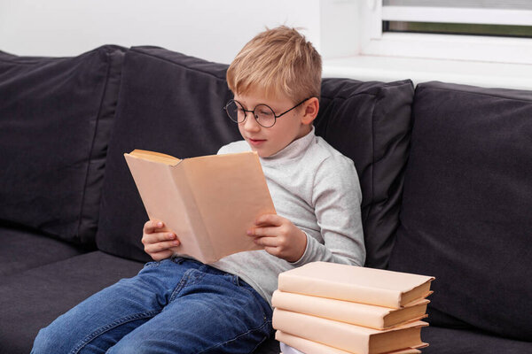 little boy with glasses and book reading from a textbook in his library