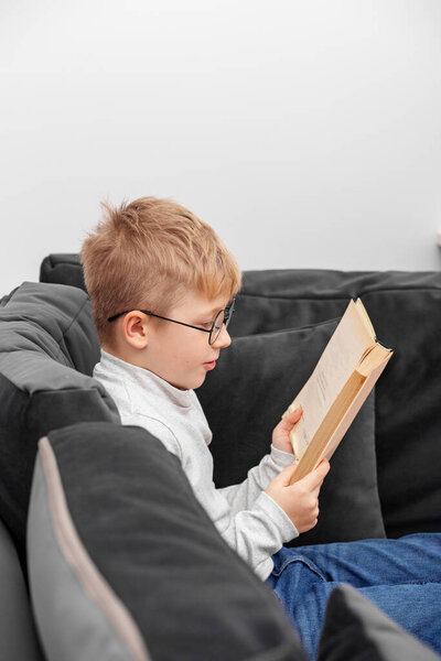 little boy reading book on sofa at home