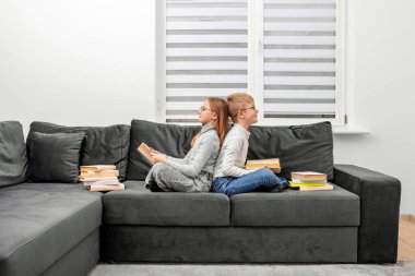 Çocuklar odadaki kanepede oturan gözlüklü kitaplar okurlar. Erkek ve kız kardeş ev ödevi çalışıyor. Dünya Kitap Günü kavramı, yaşam tarzı, öğrenim, eğitim.