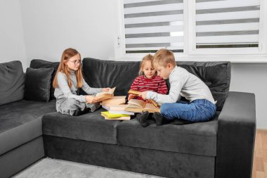 Genç kız ve küçük kızı kanepede oturup kitap okuyorlar.