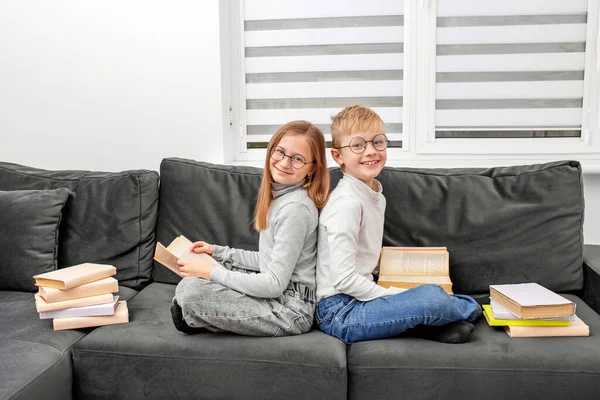 子供たちは部屋のソファに座って眼鏡で本を読みます ワールドブックデー ライフスタイル 教育のための概念 兄と妹は宿題を勉強している — ストック写真
