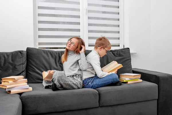 Children read books in eyeglasses sitting on sofa in room. Concept for World Book Day, lifestyle, study, education. Brother and sister are studying homework.