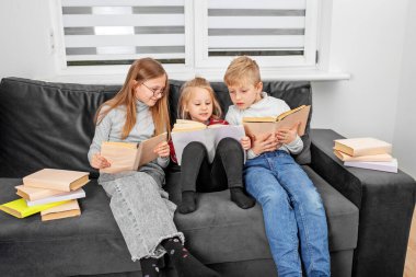 Çocuklu küçük bir kız kanepede oturmuş kitap okuyor ve oturma odasında kitap okuyor.