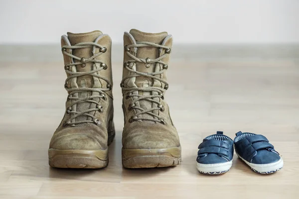 old worn military boots and baby shoes on wooden floor. Concept of military father and family.