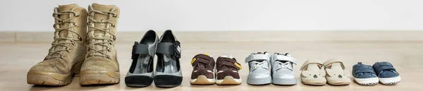 old worn military boots, women's shoes and lot of baby shoes on wooden floor. Military father and family concept.