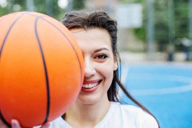 Close up. Smiling sportswoman with basketball on background of blue sports court. Sport and hobby concept.