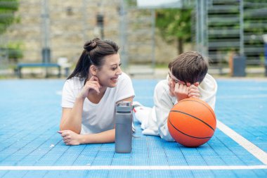 Teenage boy and girl are sitting on sports field, drinking water and talking during break.