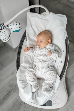 Adorable baby sleeps in baby swing in room. Newborn concept.