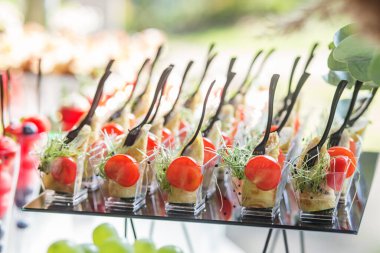 catering buffet table with snacks and appetizers. Tasty appetizers served in glass jars on a black glass stand.
