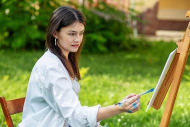 Young female artist paints picture in summer park in sunlight. Art and hobby concept.