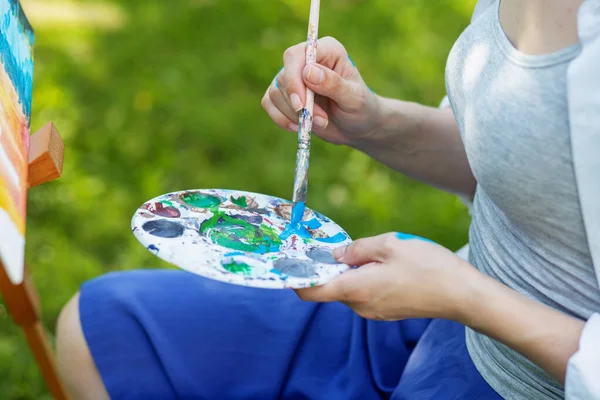 Close-up of woman\'s hand mixing paints with brush in palette at lesson in park. Art and hobby concept.