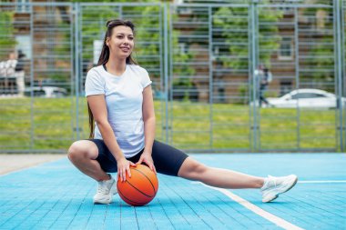 Smiling sportswoman with basketball on background of blue sports court. Sport and hobby concept. Summertime