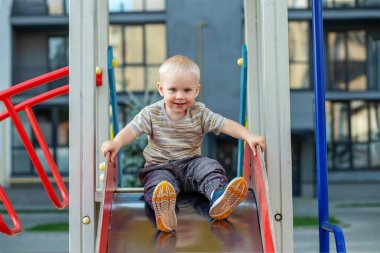 İki yaşındaki tatlı bir çocuk yaz zamanı oyun parkında slaytla oynuyor. Çocuk anaokulunun bahçesinde oynuyor. Aktif çocuk renkli kayıyor ve sallanıyor.