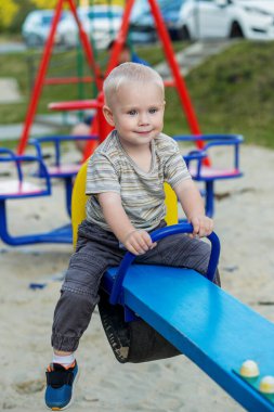Sevimli çocuk oyun bahçesinde tahterevallide eğleniyor. Sarışın çocuk yazın oyun alanında oynuyor. Anaokulu kavramı