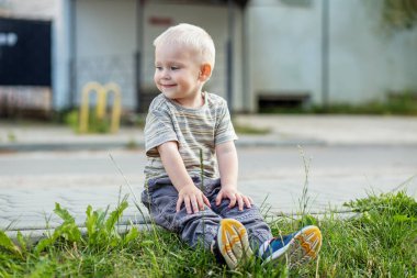 Gülümseyen çocuk parkta oturuyor. Küçük sarışın çocuk. Anaokulu, eğitim ve çocukluk kavramı