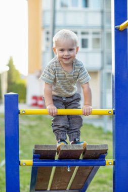 Küçük çocuk oyun parkına tırmanıyor. Dışarıda oynayan sevimli gülümseyen çocuk. Anaokulu kavramı