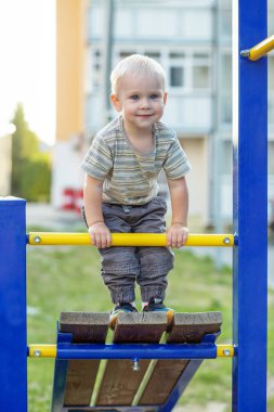 Küçük çocuk oyun parkına tırmanıyor. Dışarıda oynayan sevimli gülümseyen çocuk. Anaokulu kavramı