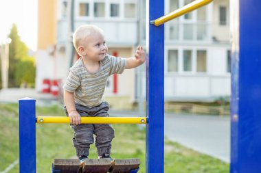 Küçük çocuk oyun parkına tırmanıyor. Dışarıda oynayan sevimli gülümseyen çocuk. Anaokulu kavramı