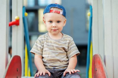 İki yaşındaki tatlı bir çocuk yaz zamanı oyun parkında slaytla oynuyor. Çocuk anaokulunun bahçesinde oynuyor. Aktif çocuk renkli kayıyor ve sallanıyor.