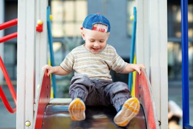 İki yaşındaki tatlı bir çocuk yaz zamanı oyun parkında slaytla oynuyor. Çocuk anaokulunun bahçesinde oynuyor. Aktif çocuk renkli kayıyor ve sallanıyor.