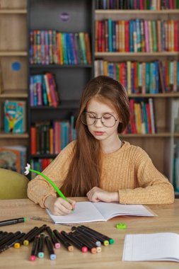 Pupil learning in school. Girl writes in copybook and does homework while sitting in library. Back to school